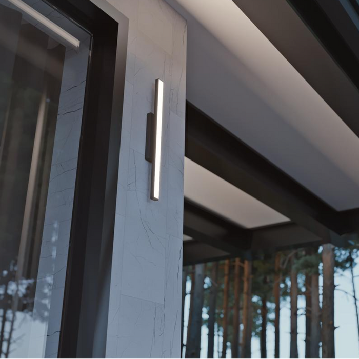 Modern outdoor light fixture on a building exterior with a forest background